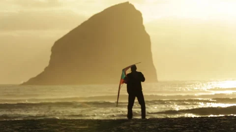 MAN SETS OFF KITE ON BEACH AT SUNSET WITH ROCK FORMATION IN BACKGROUND Stock Footage 53220713