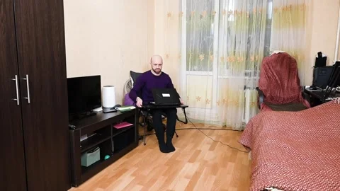 A man sets up a mini folding table for remote work with a laptop in his bedroom Stock Footage 345043958