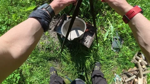 Man sets pot on tripod over grill fire Stock Footage 339613822