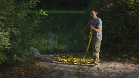 Man sets slackline between trees above the river. 스톡 동영상 140762627