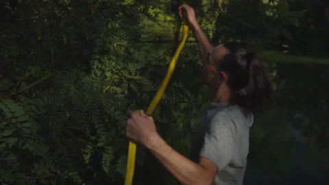 Man sets slackline between trees above the river. 스톡 동영상 140792687