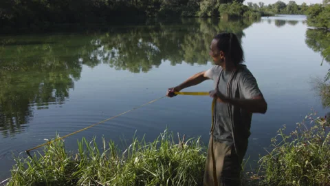 Man sets slackline between trees above the river. 스톡 동영상 140797993
