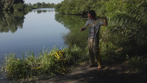 Man sets slackline between trees above the river. 스톡 동영상 140798016