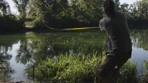 Man sets slackline between trees above the river. 스톡 동영상 140798086