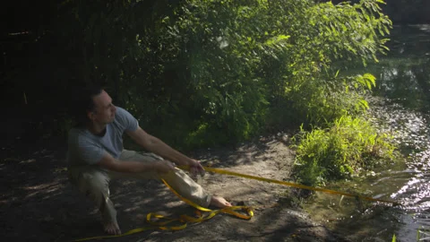 Man sets slackline between trees above the river. 스톡 동영상 140799632