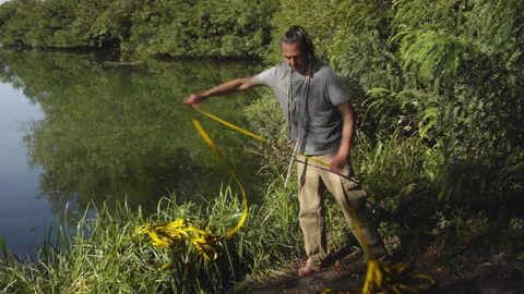 Man sets slackline between trees above the river. 스톡 동영상 140799684