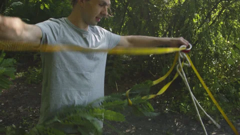Man sets slackline between trees above the river. 스톡 동영상 140806124