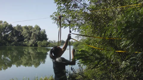 Man sets slackline between trees above the river. 스톡 동영상 140812265