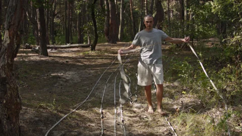 Man sets slackline between trees above the river. 스톡 동영상 140813168