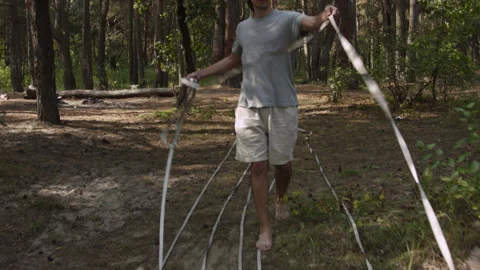 Man sets slackline between trees above the river. 스톡 동영상 140813677