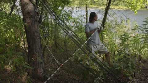 Man sets slackline between trees above the river. 스톡 동영상 140815779