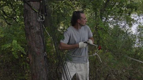 Man sets slackline between trees above the river. 스톡 동영상 140816239