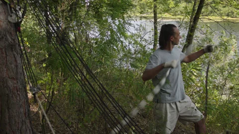Man sets slackline between trees above the river. 스톡 동영상 140816346