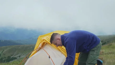 A man sets up a tent on a hike in the mountains. A tourist gathers a tent Stock Footage 230226130