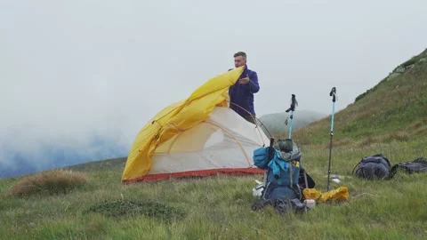A man sets up a tent in the mountains against the background of clouds Stock Footage 220095140