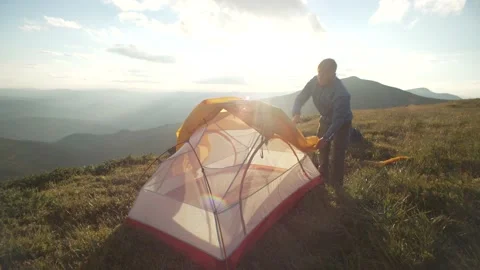 A man sets up a tent in the mountains at sunset. Camping by a tourist Stock Footage 213018611