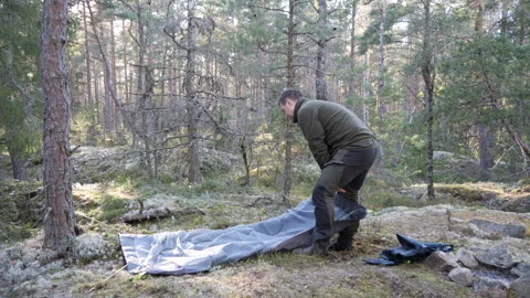 Man setting up camping tent in pine forest wilderness 動画素材 333690492