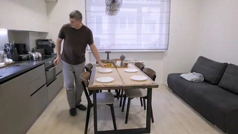 Man setting dining table with plates in modern cozy apartment kitchen Stock Footage 336307556