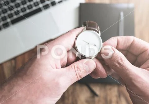 Man setting his wristwatch against laptop computer and personal organizer on Stock Photos