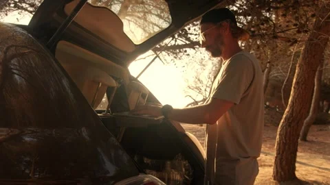 Man Setting Up Laptop in Car Trunk to Work Outdoors, Golden Backlight Stockbeeldmateriaal 341938957