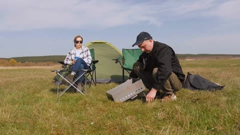 Man setting up a portable barbecue grill at a campsite Stock Footage 319791053