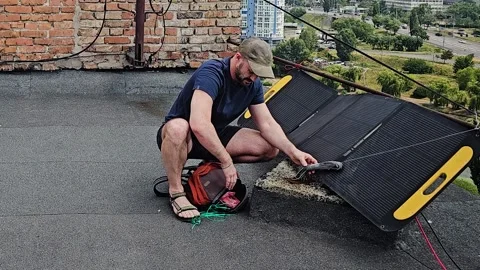 Man Setting Up Portable Foldable Solar Panel on Flat Roof for Alternative Energy Stock Footage 341083568