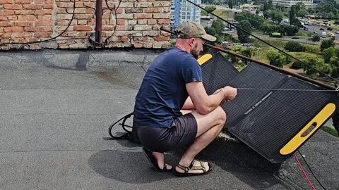 Man Setting Up Portable Foldable Solar Panel on a Rooftop for Alternative Energy Stock Footage 341663356