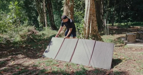 Man setting up portable solar panel in forest clearing Vídeos de archivo 331525730