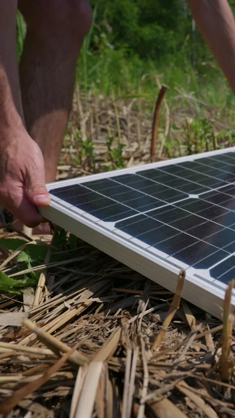 Man Setting Up Portable Solar Panel Outdoors in Sunny Grass Field Stock Footage 342184125