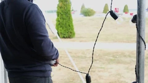 Man setting up string lights for outdoor event . Minsk, Belarus - May 10, 2023 Stock Footage 287161425