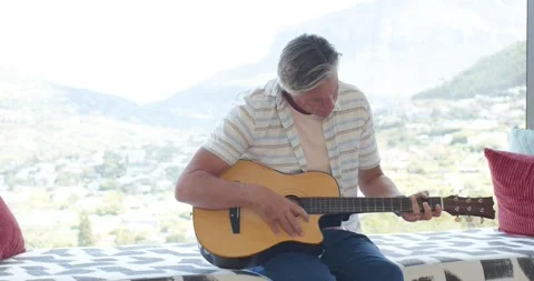 Man is settling acoustic guitar on lap, tuning and playing for relaxation on Stock Footage 339559082