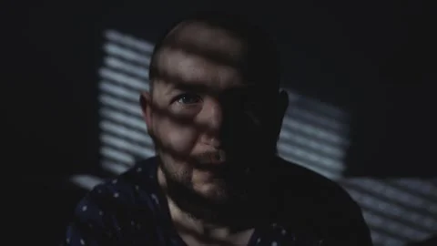 Man in the shadow of the blinds looks at the camera. Stock-Footage 274951440