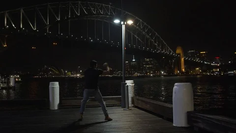 Man Shadow Boxing on Wharf in Front of Sydney Harbour Bridge at Night Stock Footage 107899831