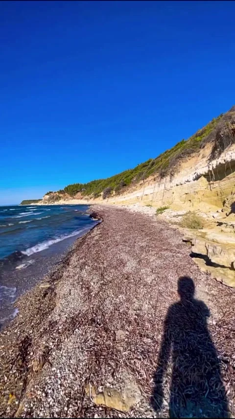 Man Shadow Walking on Stony Coastal Beach with Scenic Cliff Stock Footage 345362469