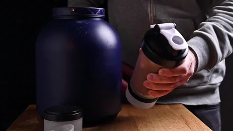 The man shakes the Sheker with a cocktail. On the table are whey protein Stock Footage 145917899