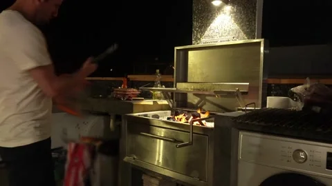 A man shaking a dustpan to draft air onto the coals of a cooking grill at a Stock Footage 173514942