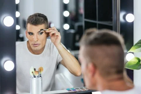 Man shaping his eyebrows while doing makeup for a show Stock Photos