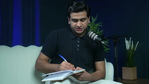 Man Sharing Notes and Speaking Into Microphone During Podcast Interview in Stock Footage 336319642