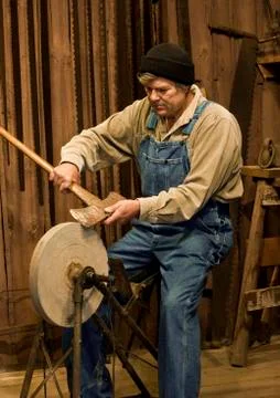 Man sharpening an axe on a grinding stone Stockfoto's
