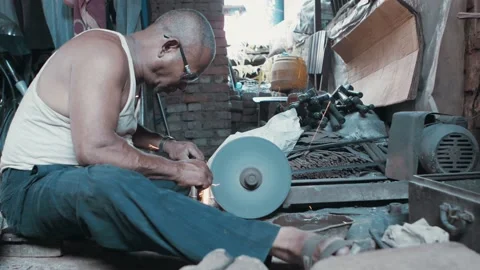 Man sharpening a metal piece on a grinder, dipping in water, steam rising Stock Footage 143610441