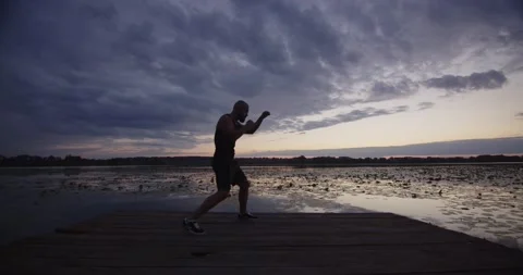 A man sharpens his strokes while playing sports on the river bank Stock Footage 229809904