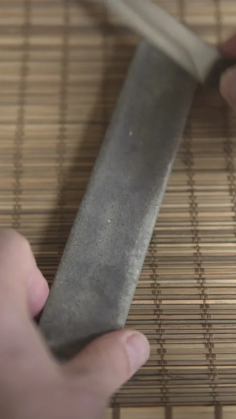 A man sharpens a kitchen knife by sliding the steel blade across a professi. Stock Footage 325795432