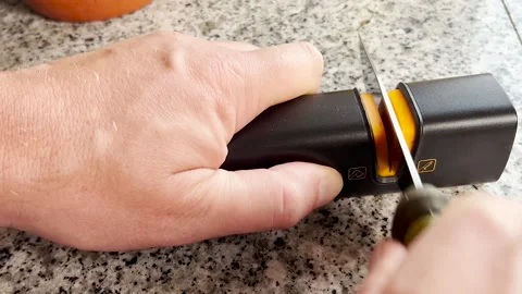 A man sharpens a kitchen knife using a handheld sharpener on a granite Stock Footage 316069659