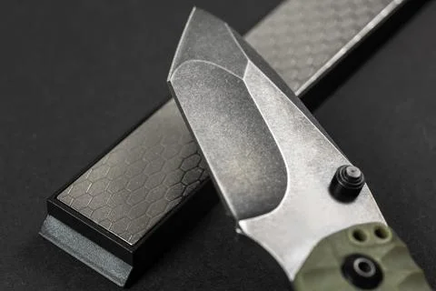 Man sharpens a knife using a whetstone on a dark table Stock-Fotos