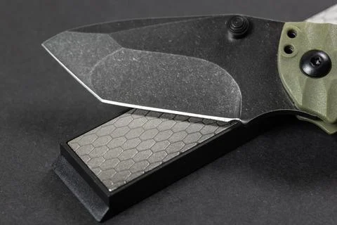 Man sharpens a knife using a whetstone on a dark table Stock-Fotos