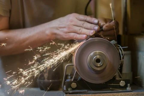 Man sharpens a metal blade on a machine. Man manufacturing in his workshop. Stock Photos