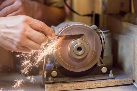 Man sharpens a metal blade on a machine. Man manufacturing in his workshop. Stock Photos