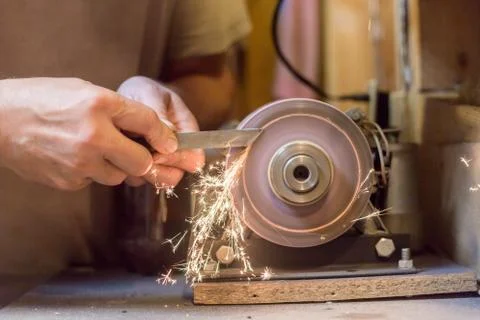 Man sharpens a metal blade on a machine. Man manufacturing in his workshop. Stock Photos