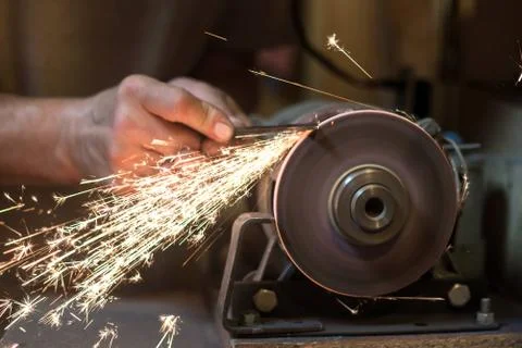 Man sharpens a metal blade on a machine. Man manufacturing in his workshop. Stock Photos