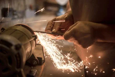 Man sharpens a metal blade on a machine. Man manufacturing in his workshop. Stock Photos